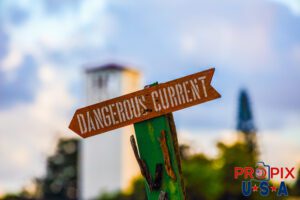 No Joke..! Dangerous current sign at Waimea bay Oahu Hawaii. The iconic tower of the Mission of St. Peter and Paul is visible behind the sign to the left.