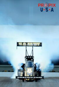 Crazy spot to take a picture... or genius..? This is now an iconic image in NHRA drag racing. Nobody had previously stood in front of a Top Fuel dragster when it was doing it's burnout. Narrowly averting getting run over, the image captured made up for the near death experience. The car was driven by NHRA 8x World Champion Tony Schumacher.